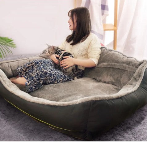 Woman sitting on a large Wooofly stone-grey bolster sofa bed with her cat in a bright, modern living room interior.