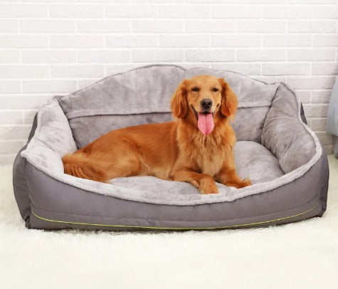 Golden Retriever resting on a Wooofly bolster-style sofa bed in stone-grey fabric against a white brick wall.